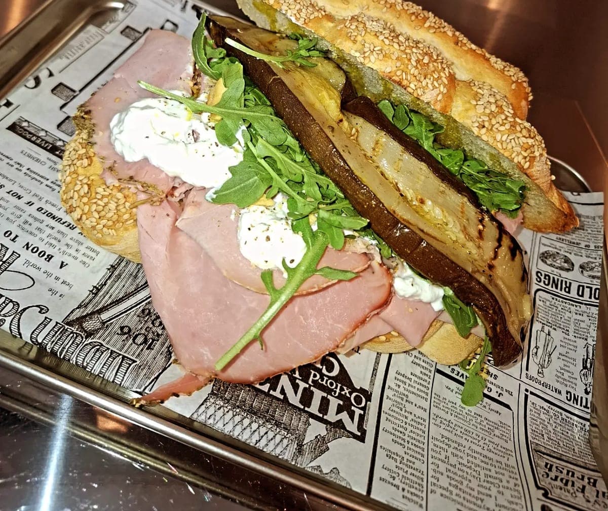 Une mafalda au sésame ouverte, garnie de jambon cuit, de stracciatella, de courgettes grillées et de roquette