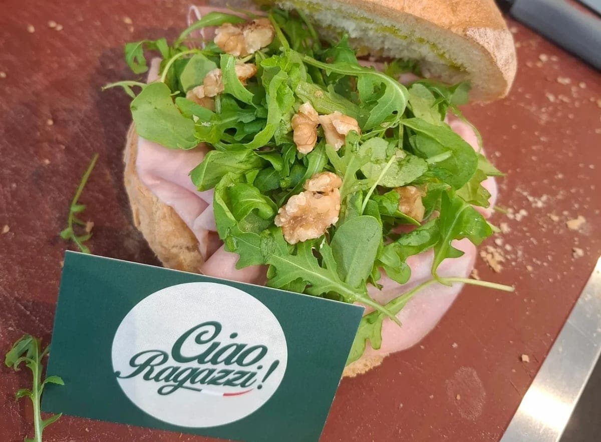 Mortadelle, roquette et cerneaux de noix sur un pain ouvert, avec une carte de visite Ciao Ragazzi! posée devant