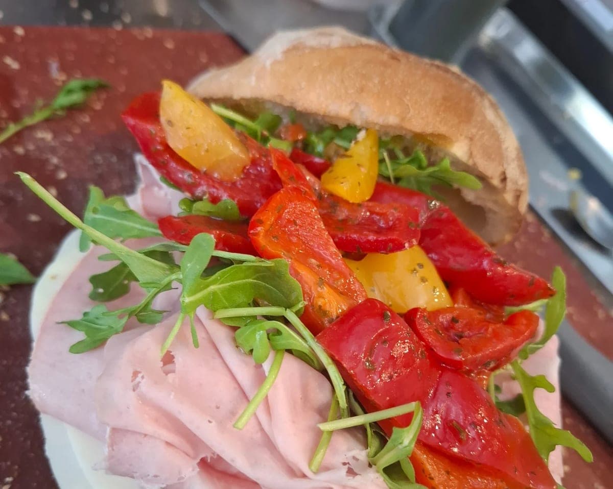 Mortadelle en tranches, roquette et poivrons rouges et jaunes grillés, dressés sur la planche avant fermeture du pain